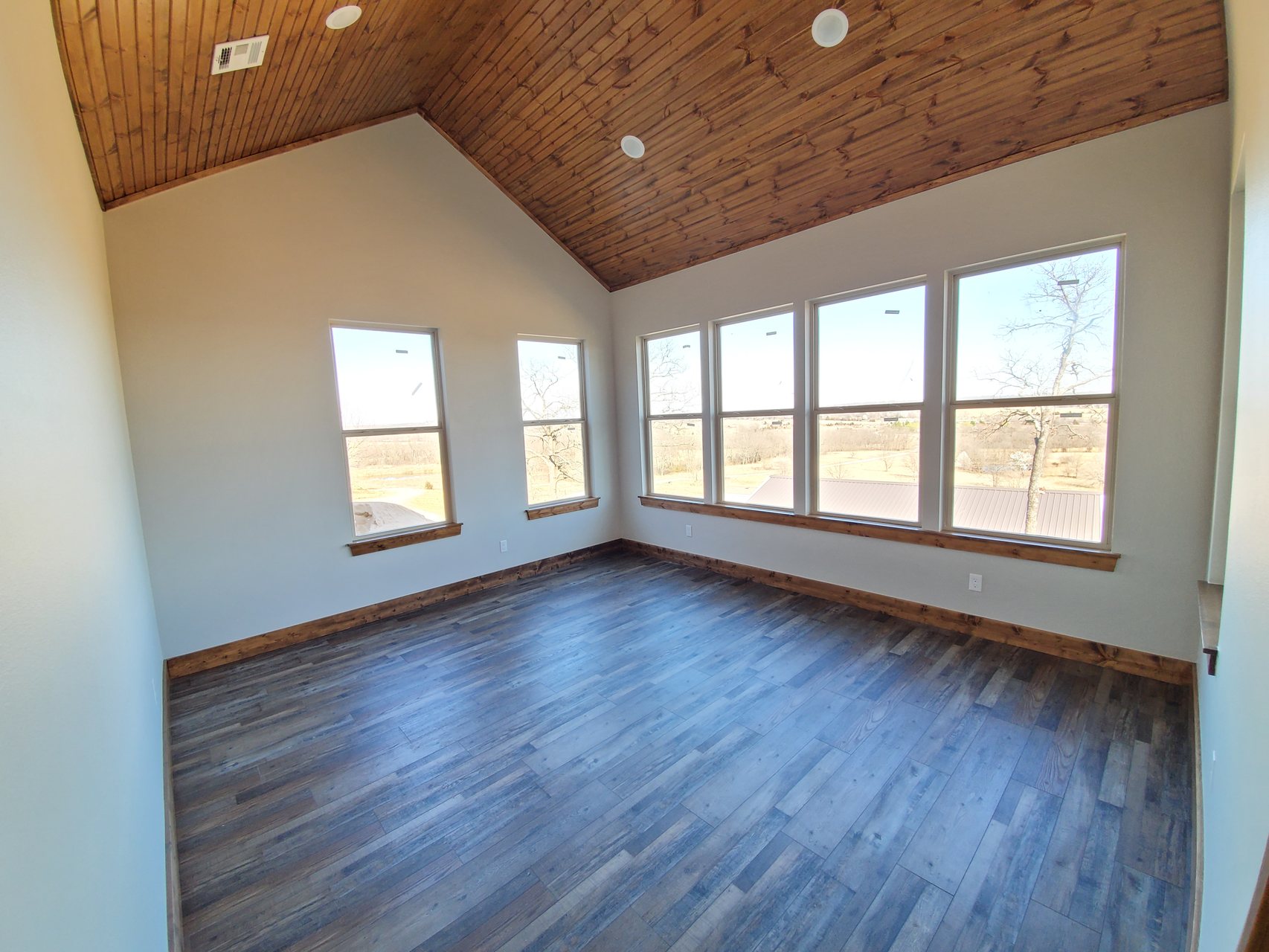 Bedroom with vaulted wood ceiling and windows overlooking Green Country land