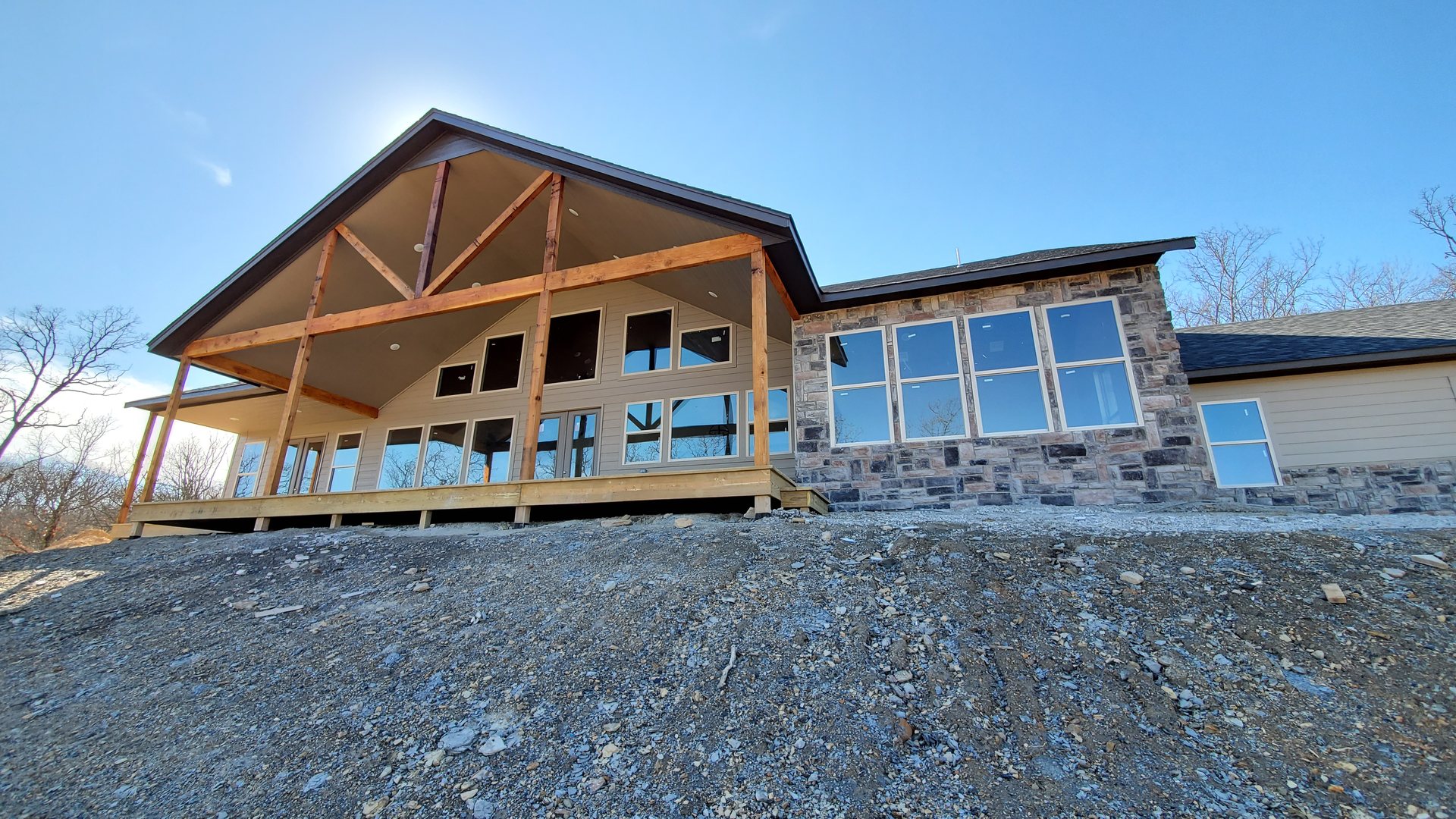 Custom lake home with stone exterior and timber-framed covered porch under construction